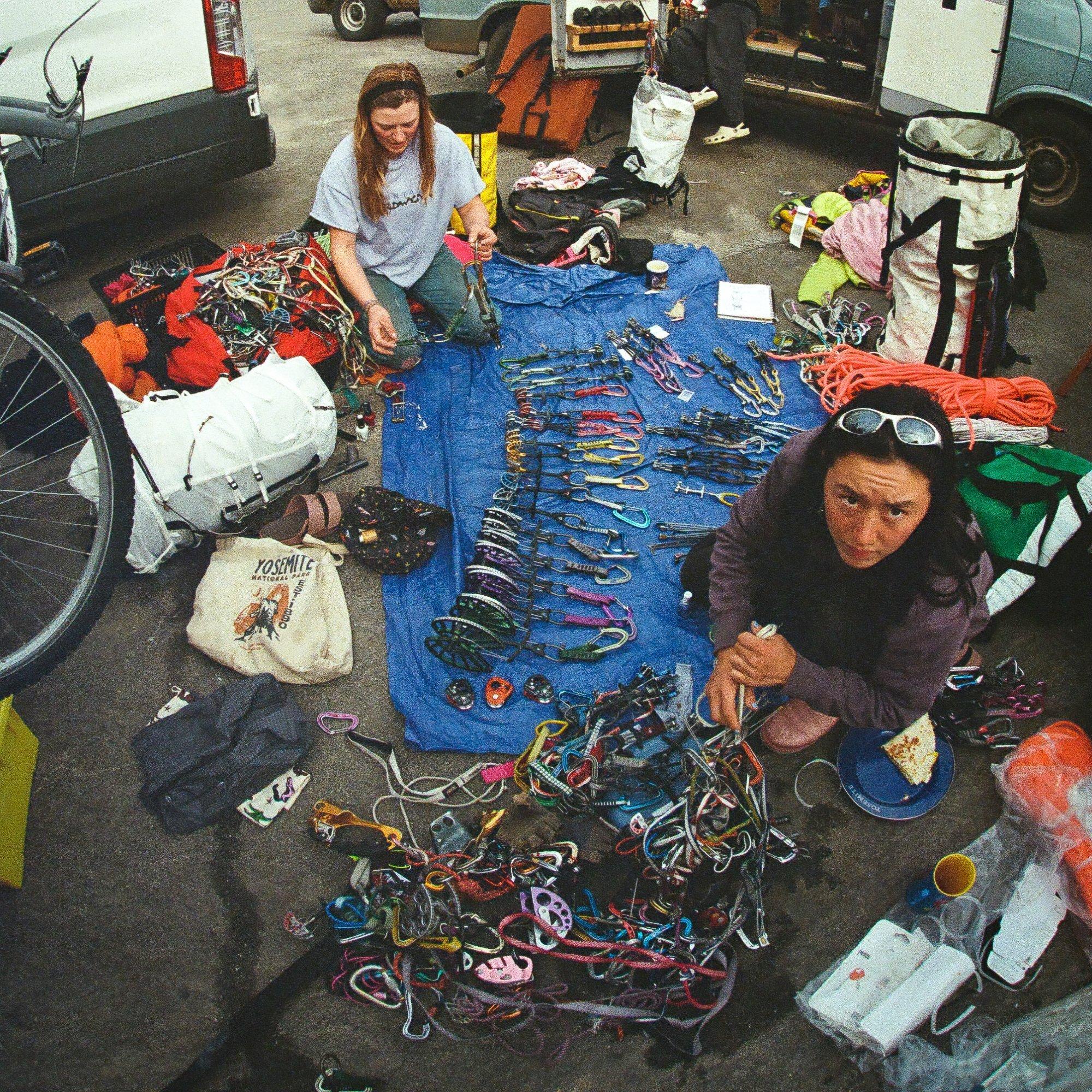 Professional climbers Flavie Cardinal and Rell Lennox organize gear splayed across a tarp, with packs, snacks, and more strewn around the area.