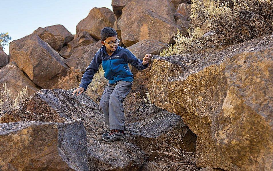 A boy climbs down a hiking trail through large boulders with a smile on his face. 