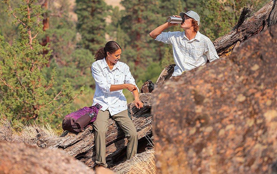  A woman rolls up her sleeve while a young man next to her takes a sip from his water bottle as the two hikers pause on the trail.  