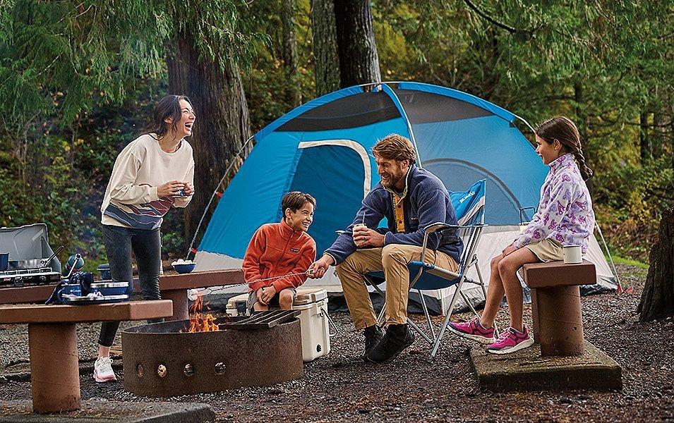 A family gathers around a fire tent with their tent pitched behind them.
