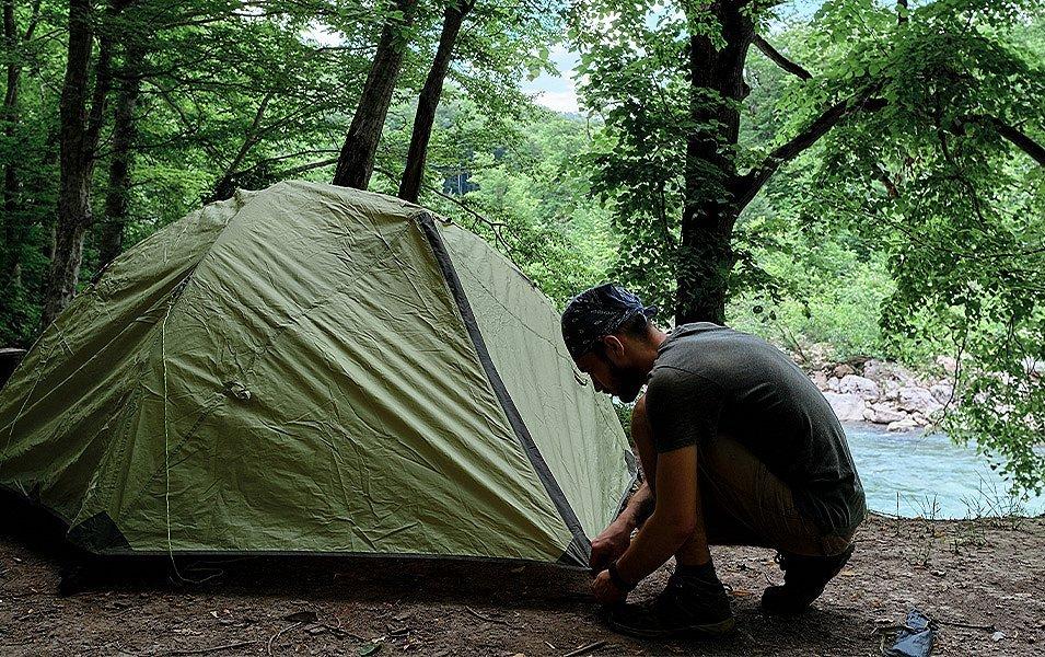A man carefully zips up his tent fly to keep out mosquitoes and bugs