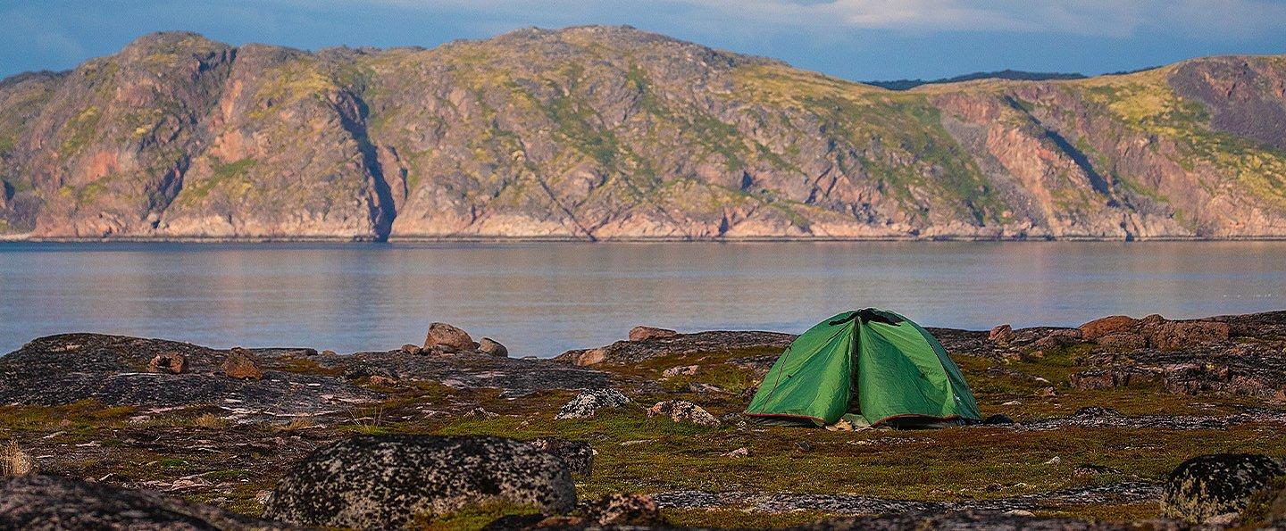 A lone green tent is pitched on a flat, grassy area, a safe distance from the lake's shoreline.