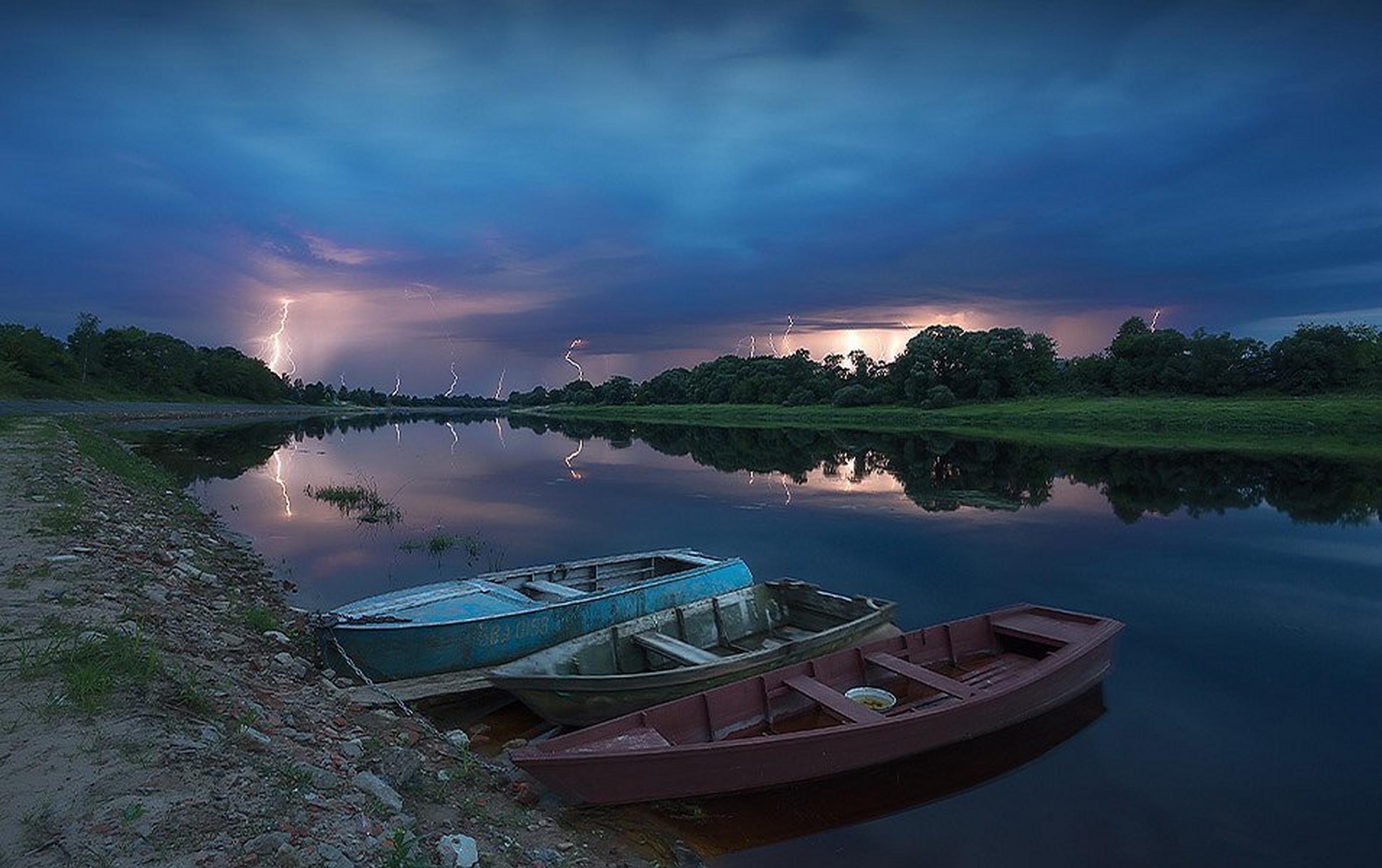 Lightning striking in the background over the water with some empty boats docked in the foreground