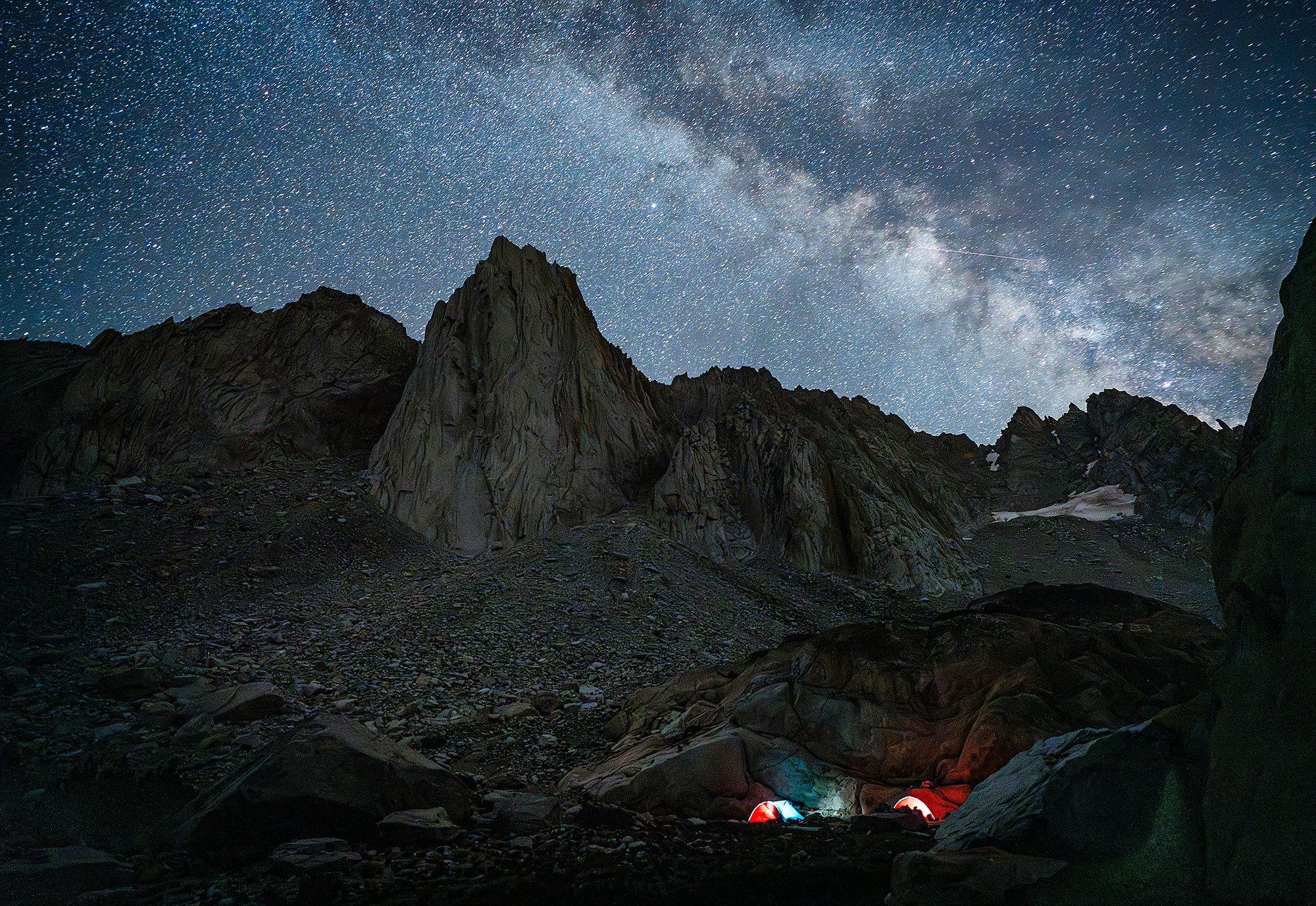 Tents at camp lit up by headlamps with a nightsky chockfull of stars above.