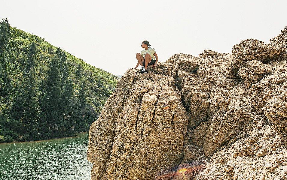 Woman sitting on rock outcropping over lake. 