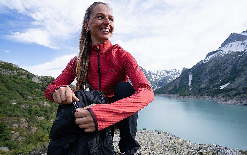 Crouched on a flat rock high above a glacial lake, a woman unzips her daypack.