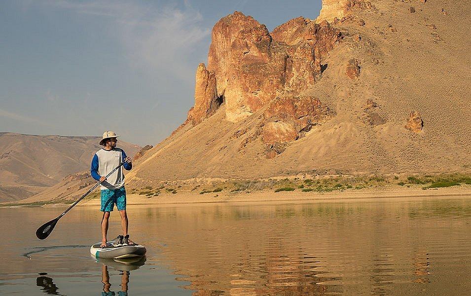 A man looks toward the shore in a beautiful canyon as he wnjoy sthe afternoon on a stand-up paddleboard. 