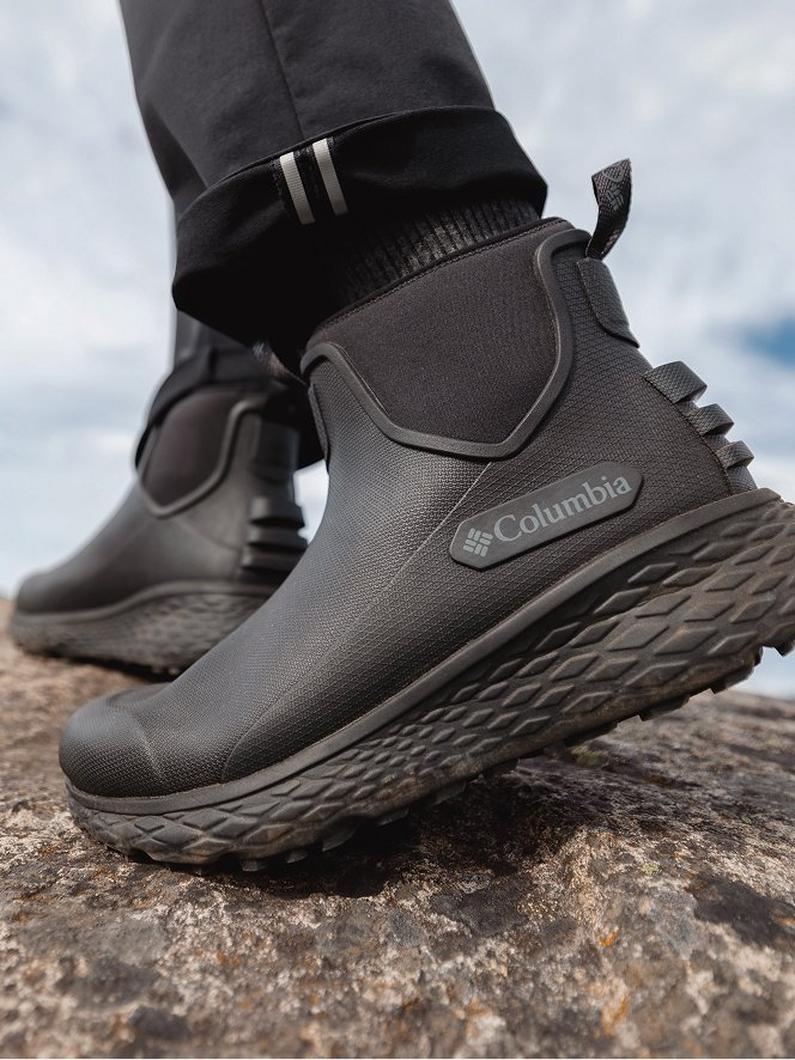 Person walking on rocky terrain wearing black waterproof ankle boots with textured rubber soles.
