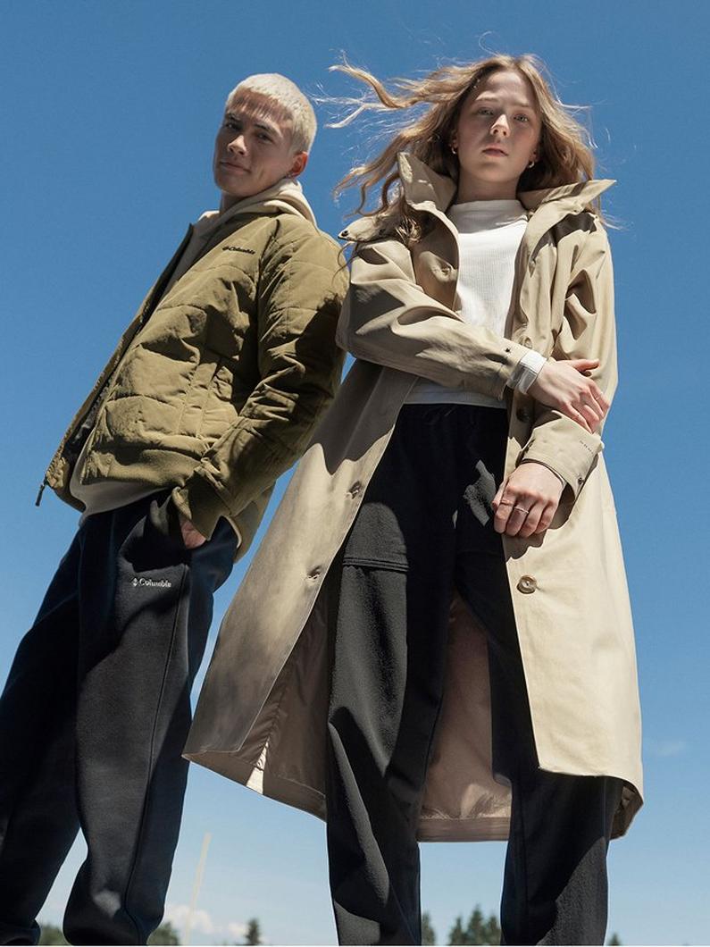 Two models standing back-to-back wearing puffer jacket and trench coat with wind blowing through their hair.