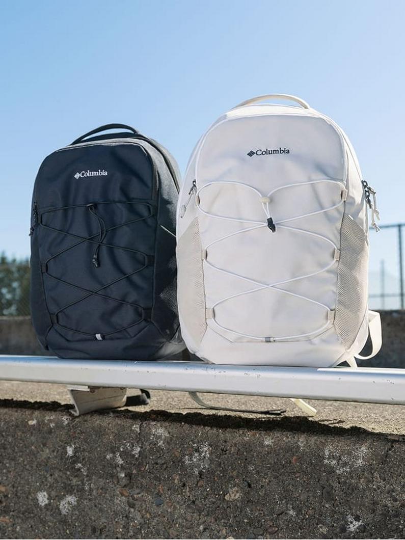 Two backpacks with elastic cord front pockets and mesh side pockets, one navy and one beige, on a railing.