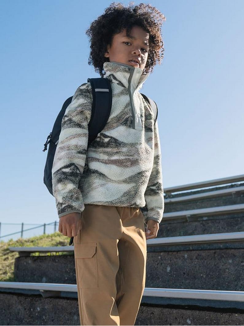 Child wearing a striped fleece pullover and tan cargo pants with a backpack, standing outdoors.