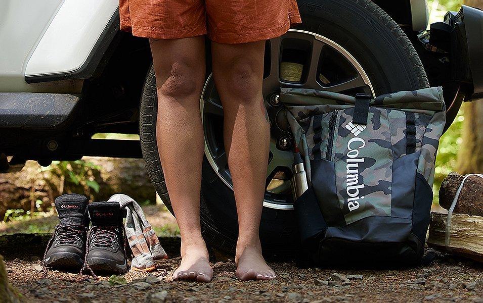 Hiker's bare feet next next to Columbia Hiking boots and Columbia hiking backpack. 