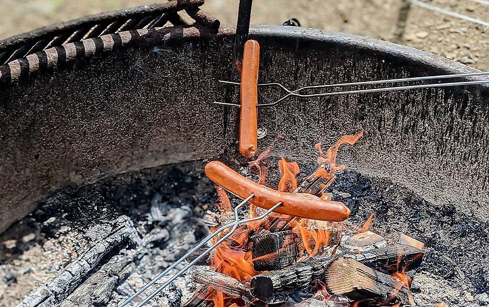 Hot dogs being cooked over fire pit. 