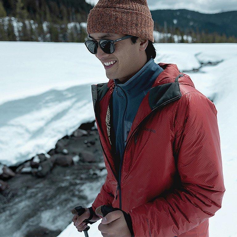 A man in a red Arch Rock Double Wall Elite insulated jacket hiking in a snowy forest.