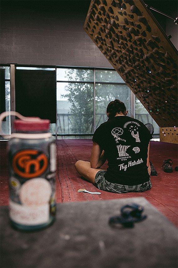 Kyra sitting on the ground of the gym, taking a break, wearing her custom champion tee