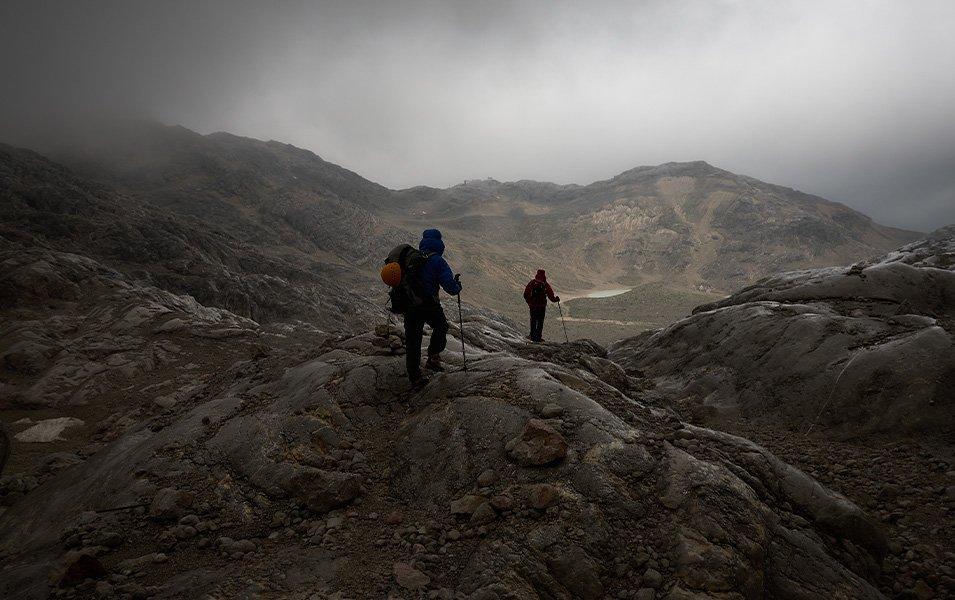 Weather moves in as two hikers continue through the fog toward an alpine lake. 