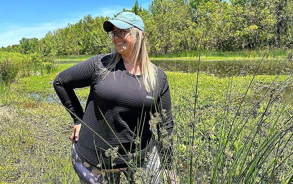 Chelsea McCurdy stands amid green foliage in Allsopp Park, Arkansas, wearing Columbia Sportswear’s Leslie Falls long sleeve hiking top. 
