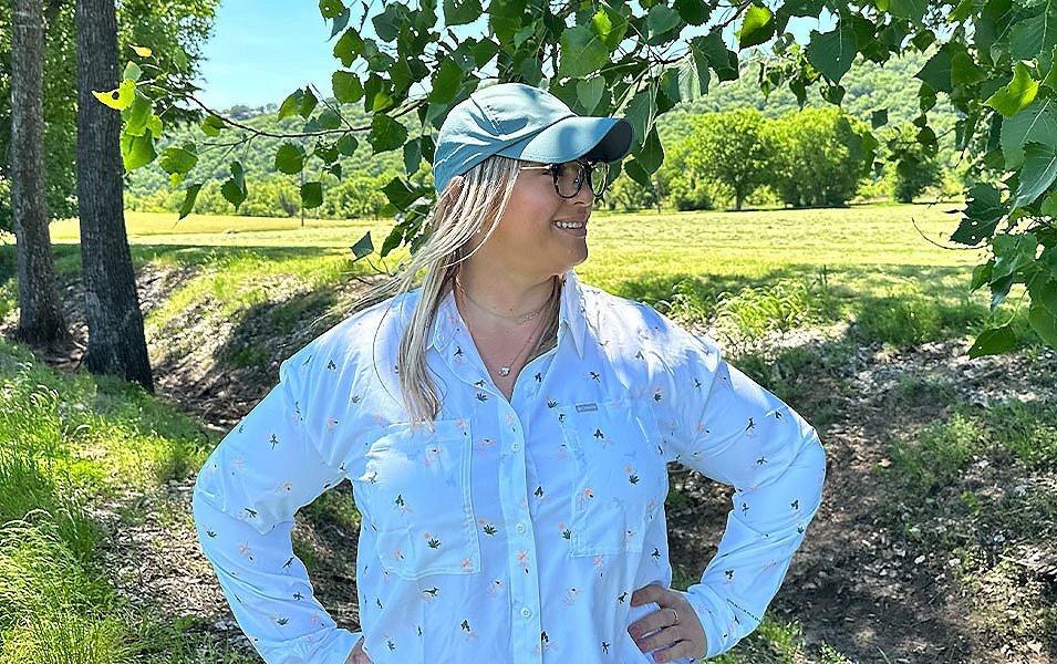 Chelsea McCurdy stands in a sunny field with trees all around her wearing Columbia Sportwear’s Silver Ridge Utility shirt. 