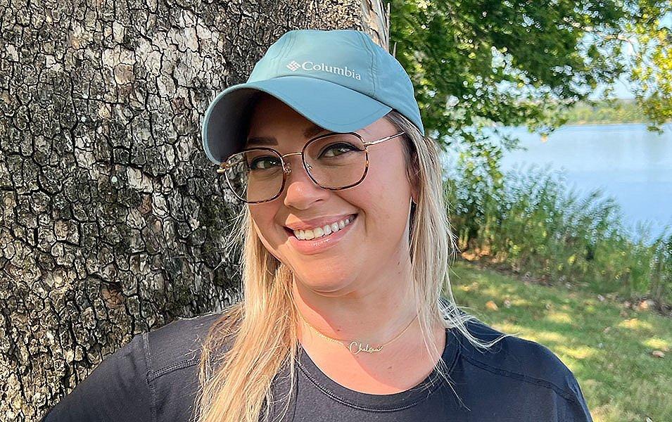 Chelsea McCurdy smiles widely for the camera at Yellowstone National Park wearing a Columbia Sportwear Coolhead II ball cap with a beautiful lake behind her. 