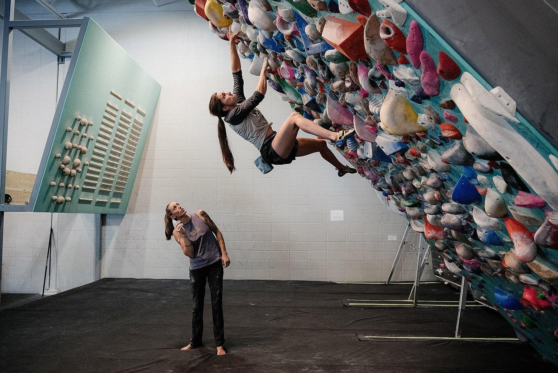 In the gym, Kyra bouldering with Alex on the sideline coaching