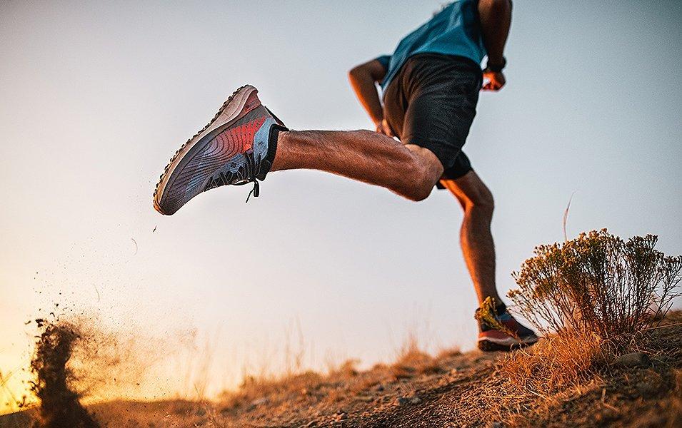 A close-up shot of a trail runner’s legs as he jogs by wearing blue-and-orange Columbia Sportswear shoes and a blue t-shirt.