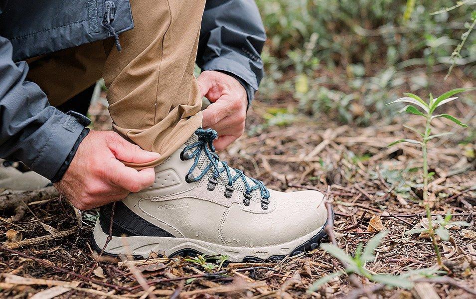 A person adjusts their pants to fit over a Columbia hiking boot.
