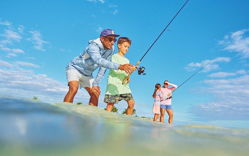 Two children have fun learning to fish with their parents. They are outfitted for a day of saltwater fishing in sun-protective apparel.