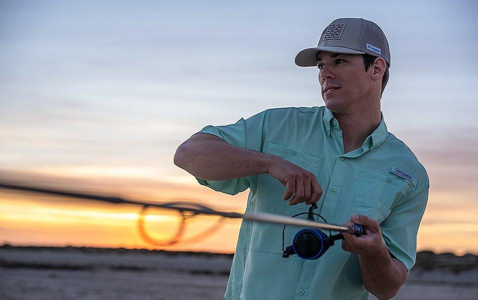 As the sun sets, a man with a reel slowly takes in his fishing line. 