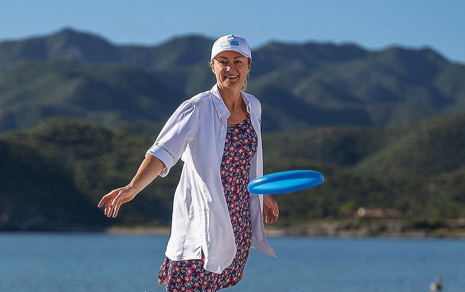 A woman with hills and a lake in the background, tosses a frisbee.