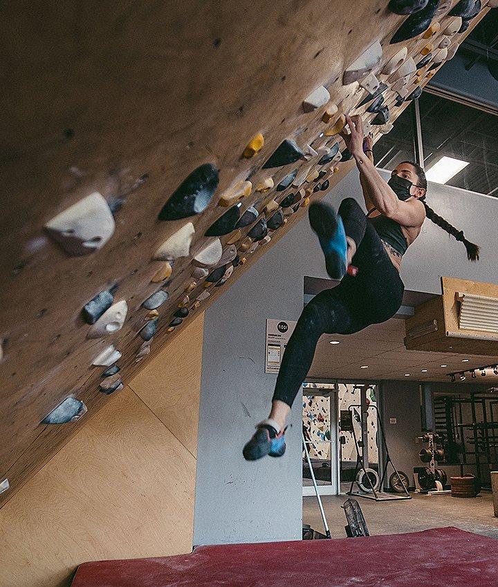Kyra bouldering, swinging her leg up to the next move in the gym