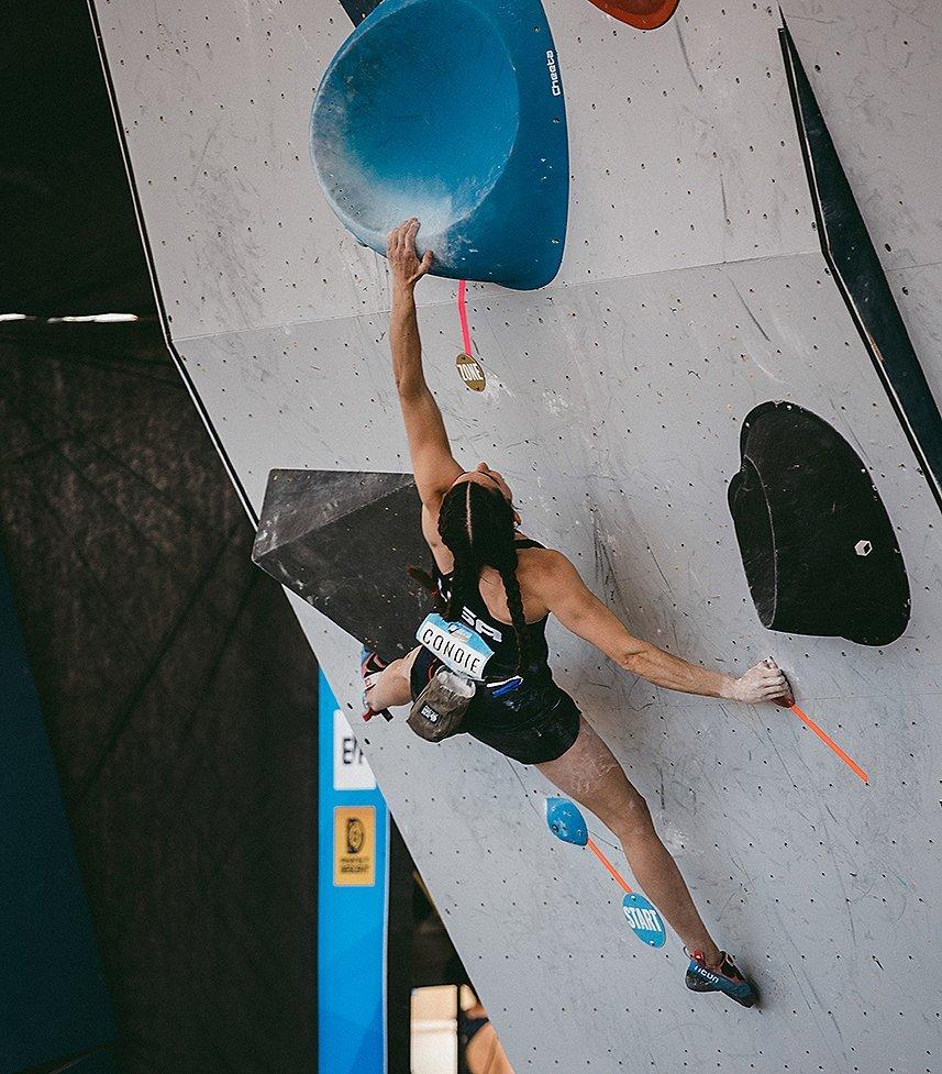 Kyra bouldering in competition, reaching for the next big hold
