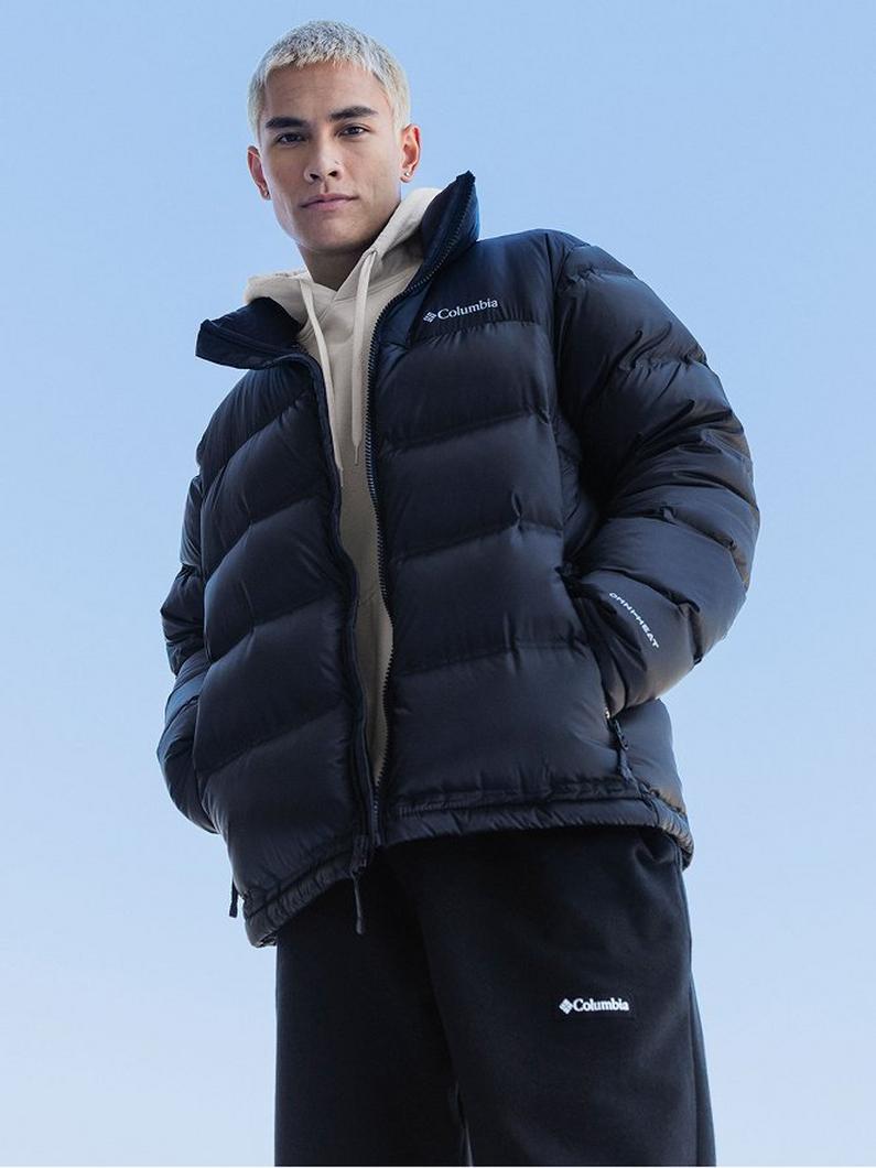 Model wearing navy puffer jacket over beige hoodie with hands in pockets.