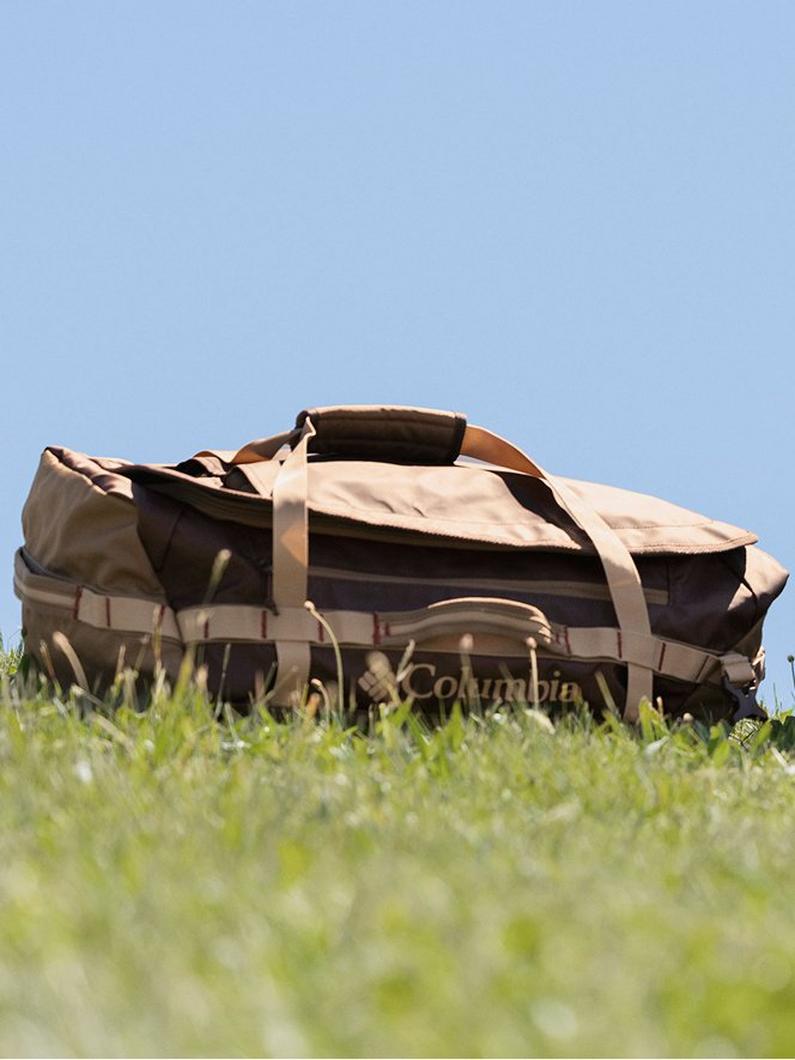 Two-tone brown and beige duffel bag with handles and straps resting on grass outdoors.