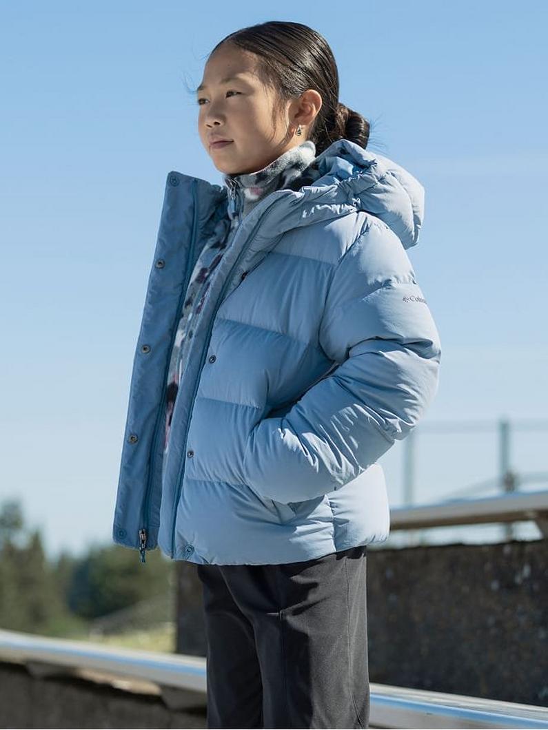 Young person wearing a blue quilted hooded puffer jacket outdoors on a clear day.