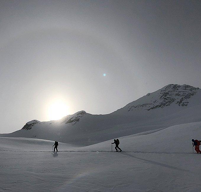 Sun setting over two people skinning in the snow up in the mountains