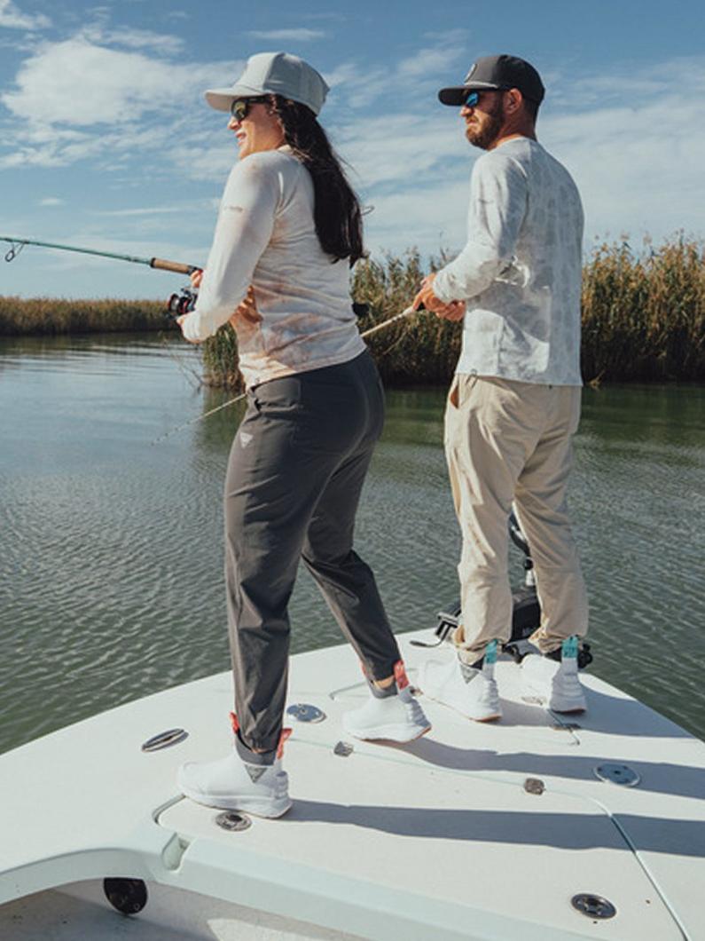 Two people fishing from a boat wearing sun-protective clothing, hats, and sunglasses on a sunny day.