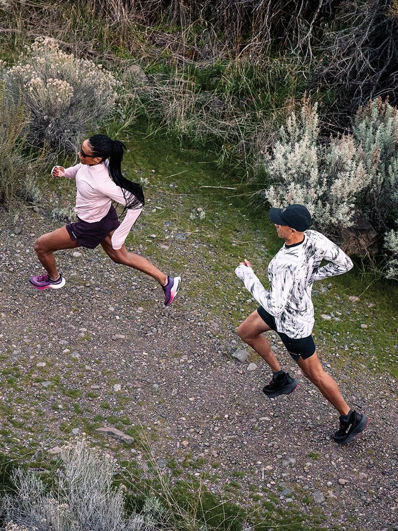 Two people running on a gravel trail surrounded by natural vegetation and brush.
