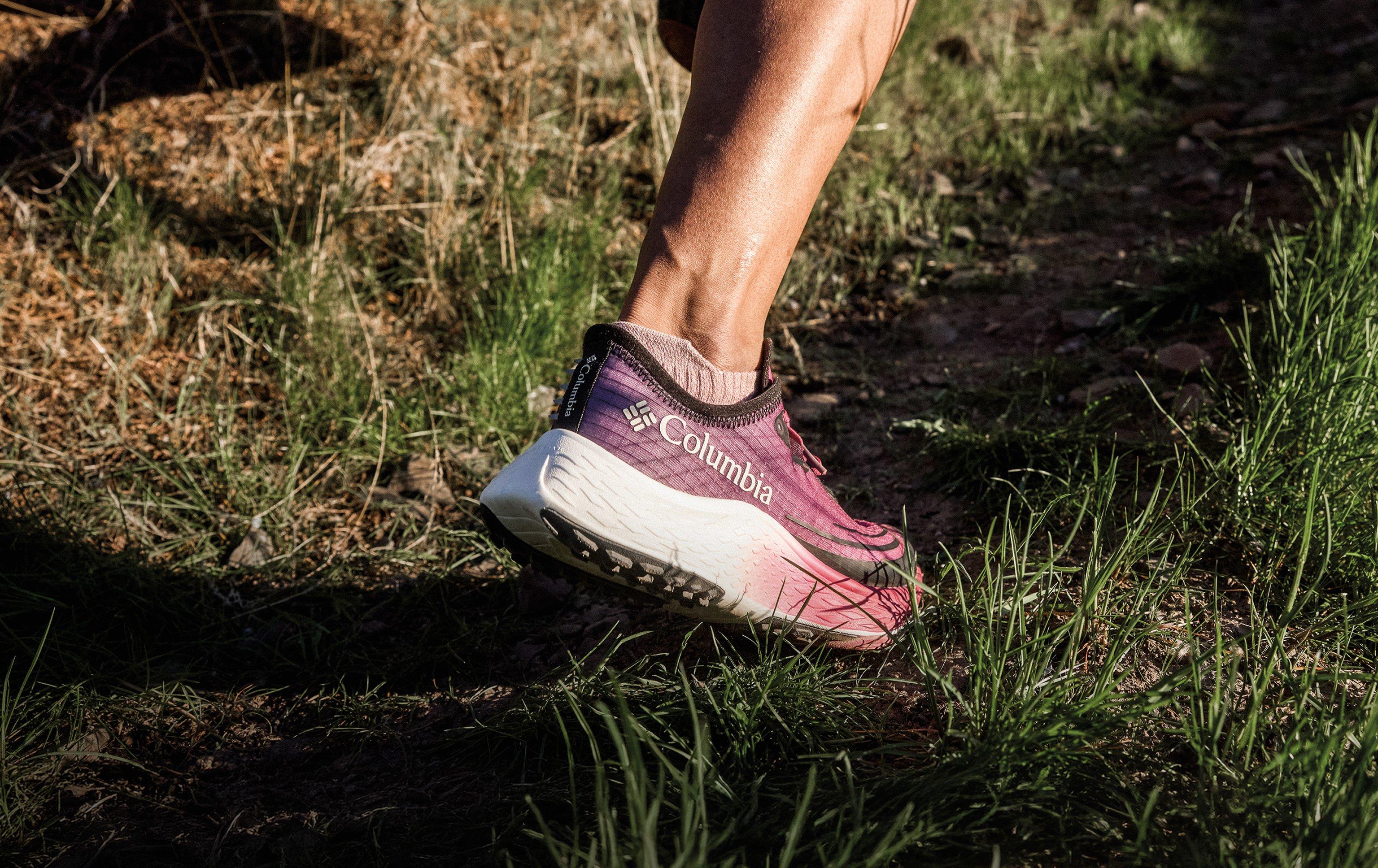 Person trail running in purple and pink athletic shoe on outdoor terrain with grass and dirt.
