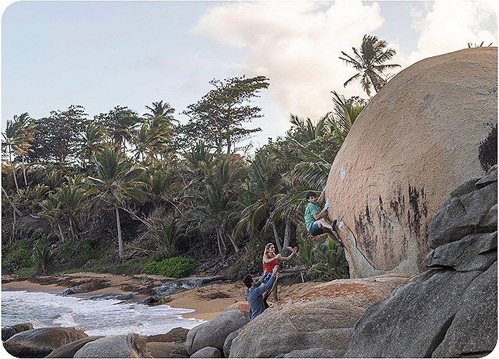 Josh Larson bouldering on the beach in Puerto Rico while Kyra Condie and another climber watch and are there for support