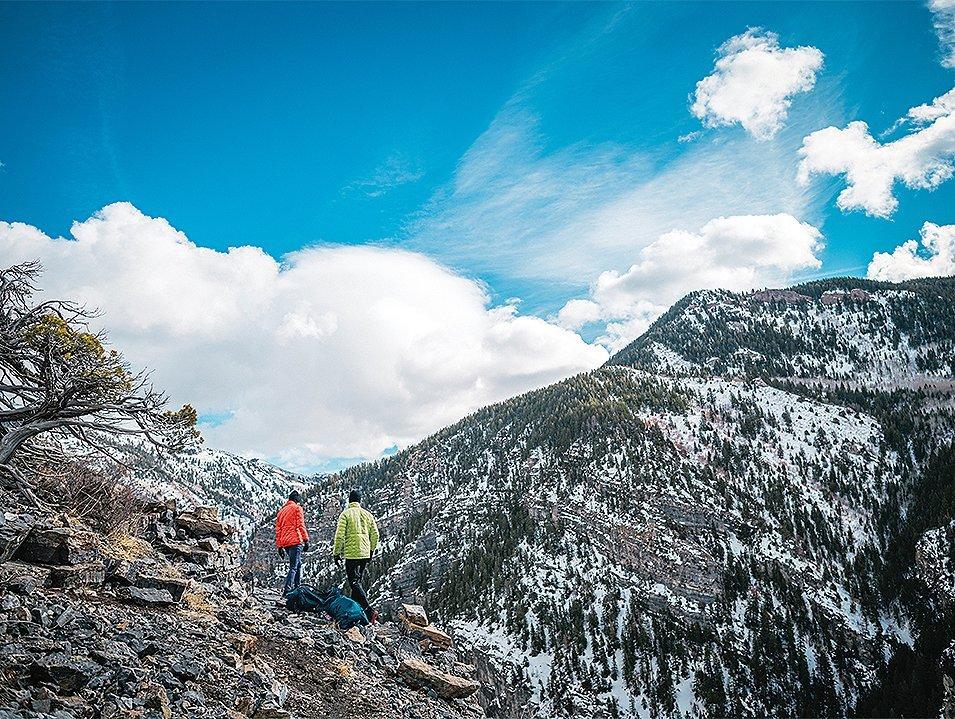 A pair of hikers walk through the mountains on a scenic trail. 