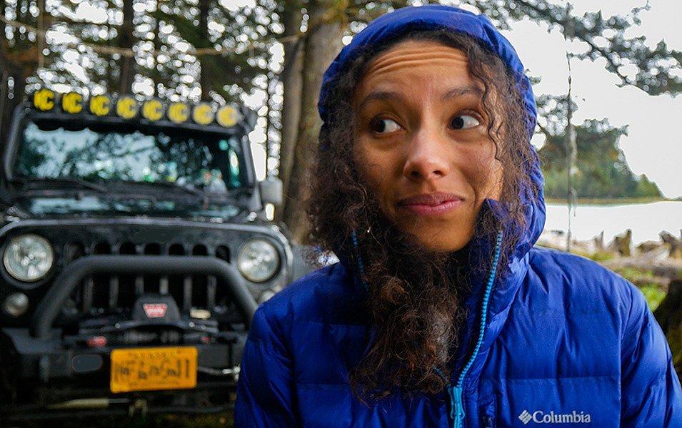 A woman stands in front of a Jeep on an overlanding excursion wearing a blue Columbia Sportswear jacket. 