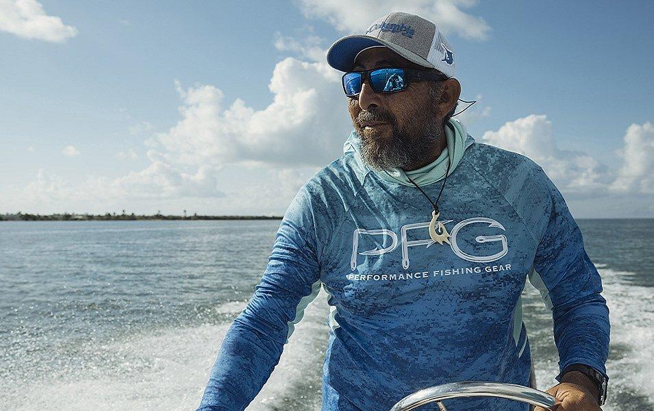 A bearded man wearing a ball cap and sunglass is driving a boat.