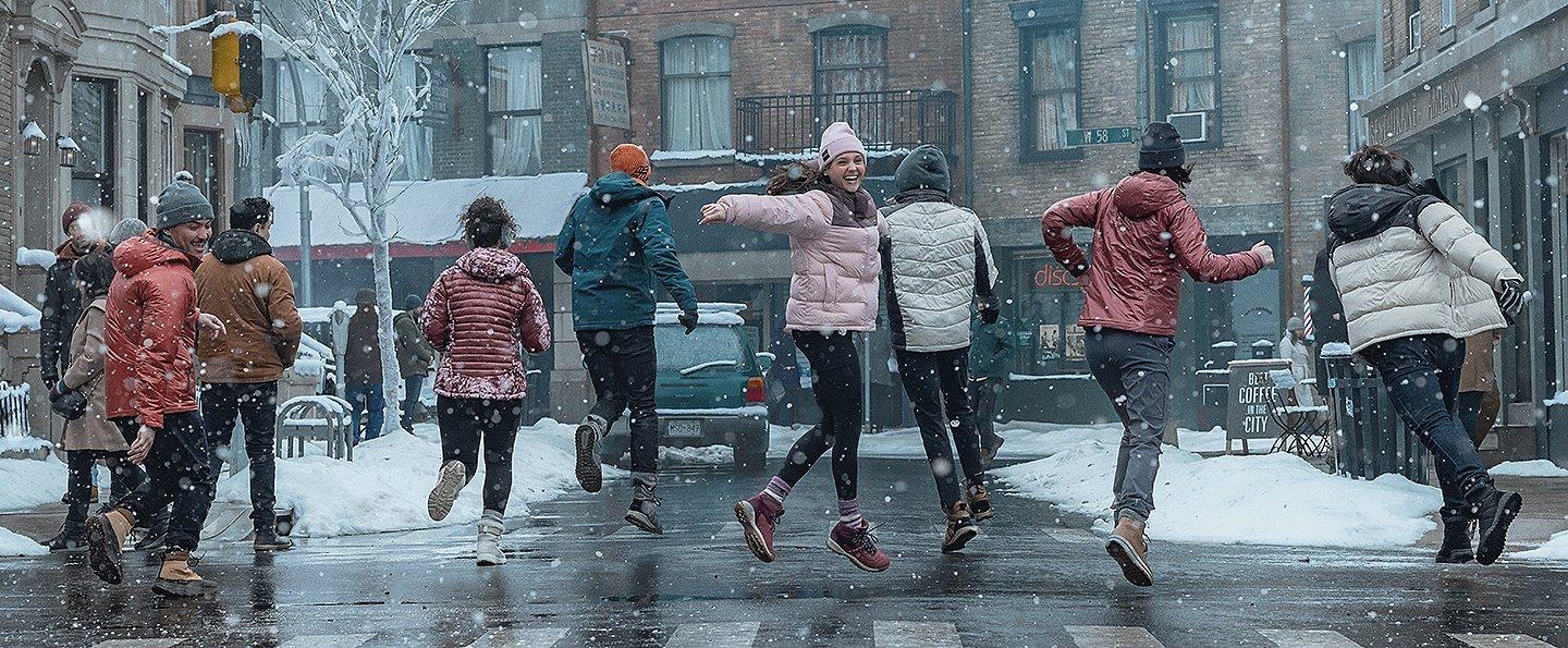 A group of friends wearing Omni-Heat Infinity jackets runs through a snow-covered street smiling, laughing, and having a good time. 