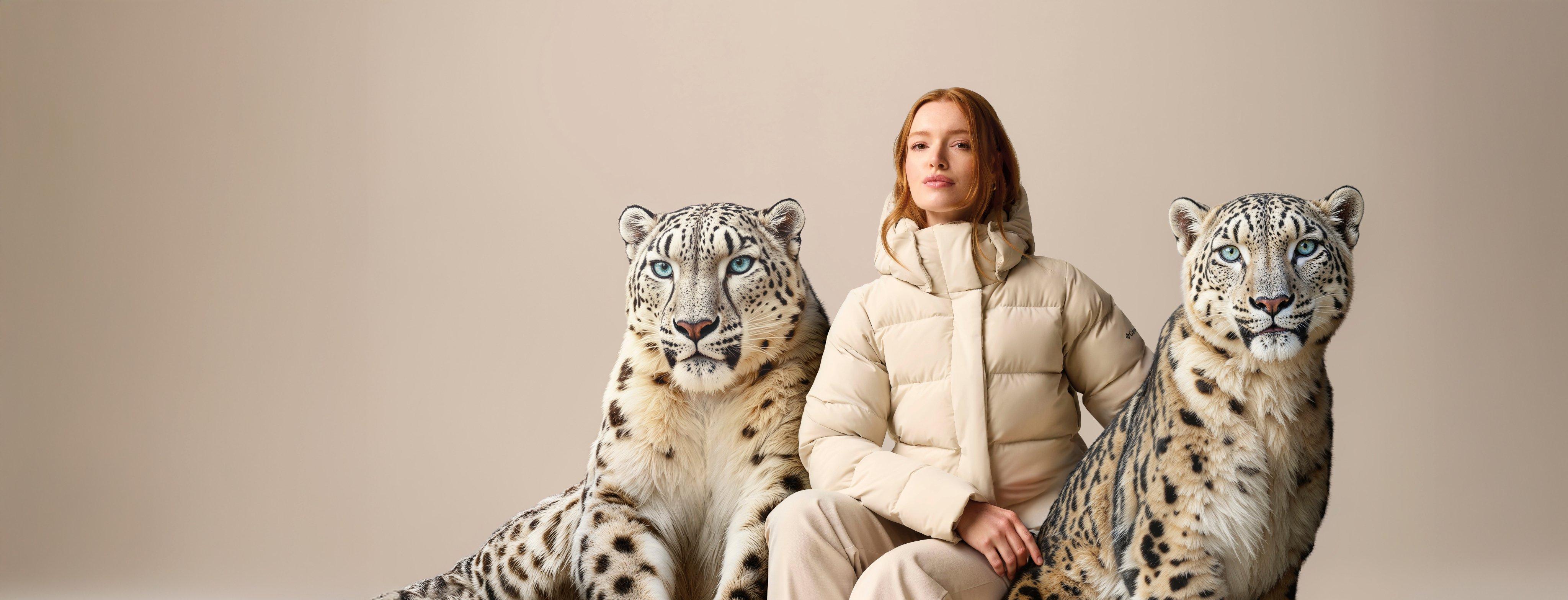 A woman in a white Amaze Puff jacket sitting next to two AI-generated snow leopards.