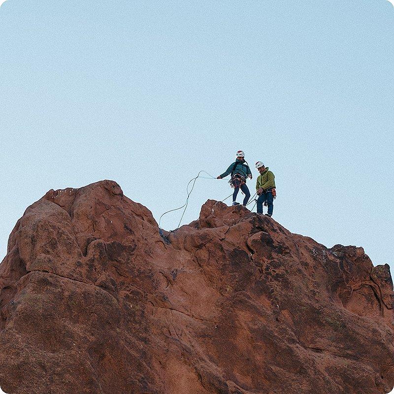 Two climbers getting ready to repel off their climb at the top of the rock face