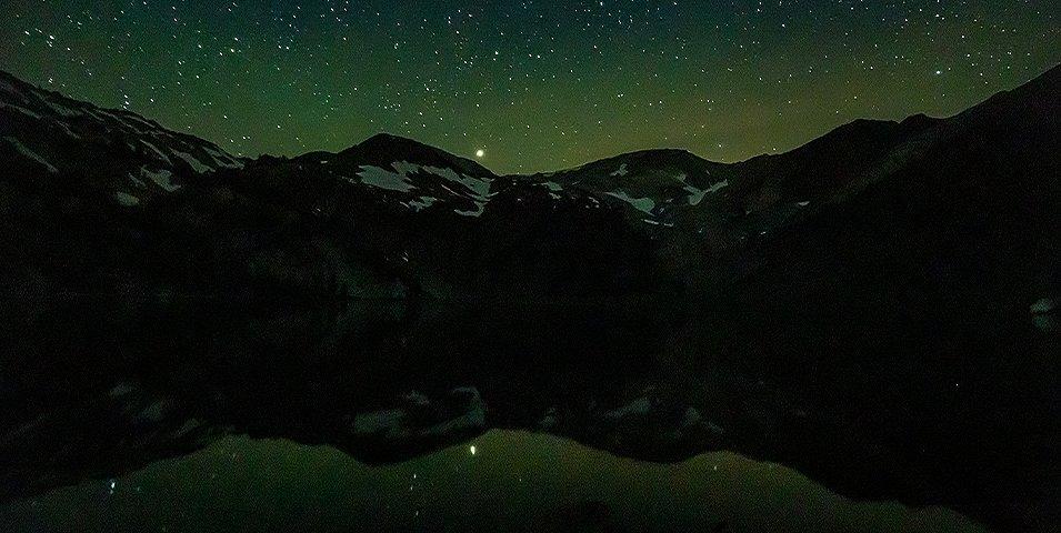 A starry sky above mountains and a lake.
