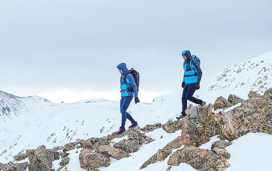 Two hikers wearing blue puffy jackets walk down a rocky trail deep in the mountains.