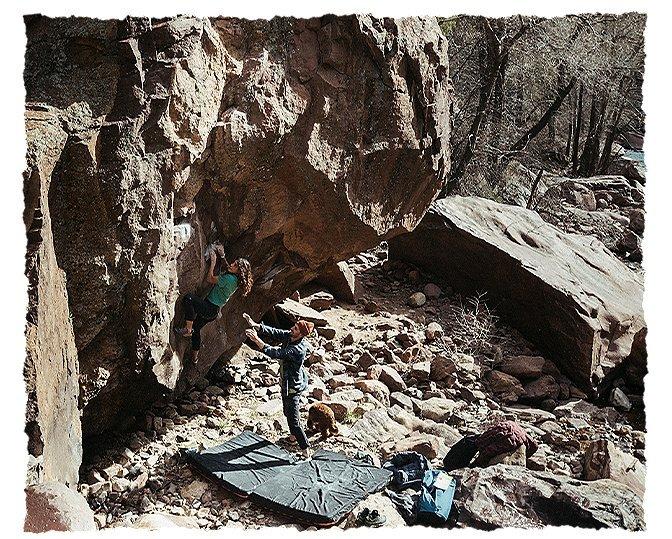 A female boulder works on her problem with MHW athlete Jon Glassberg ready on the catch