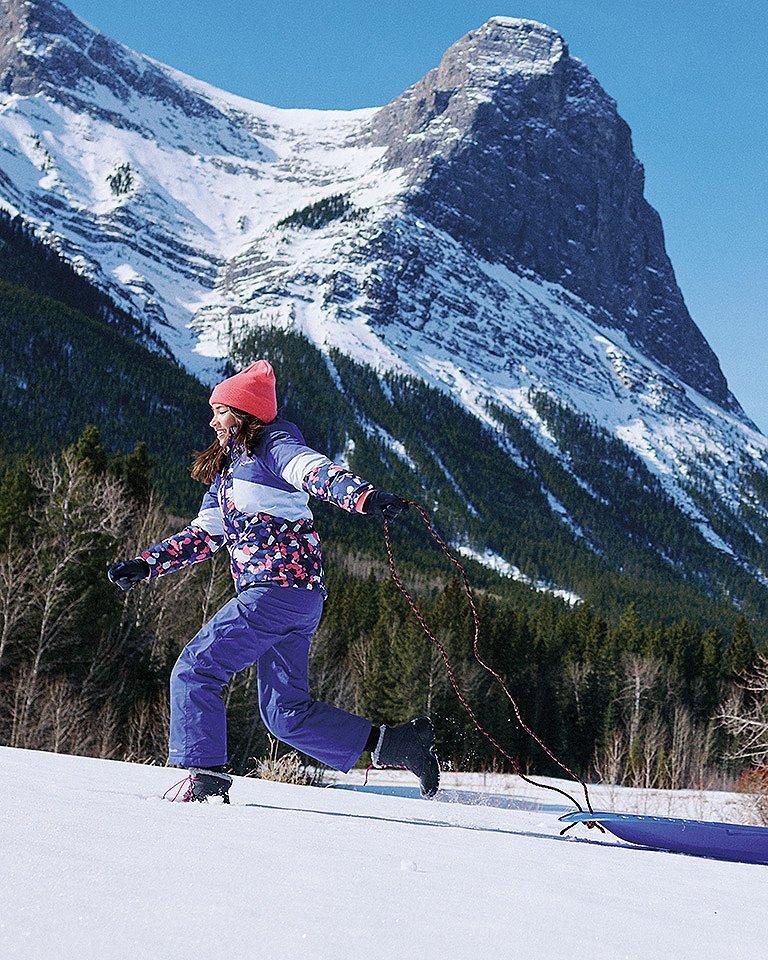 A woman having fun in the snow with a beautiful mountain in the background.