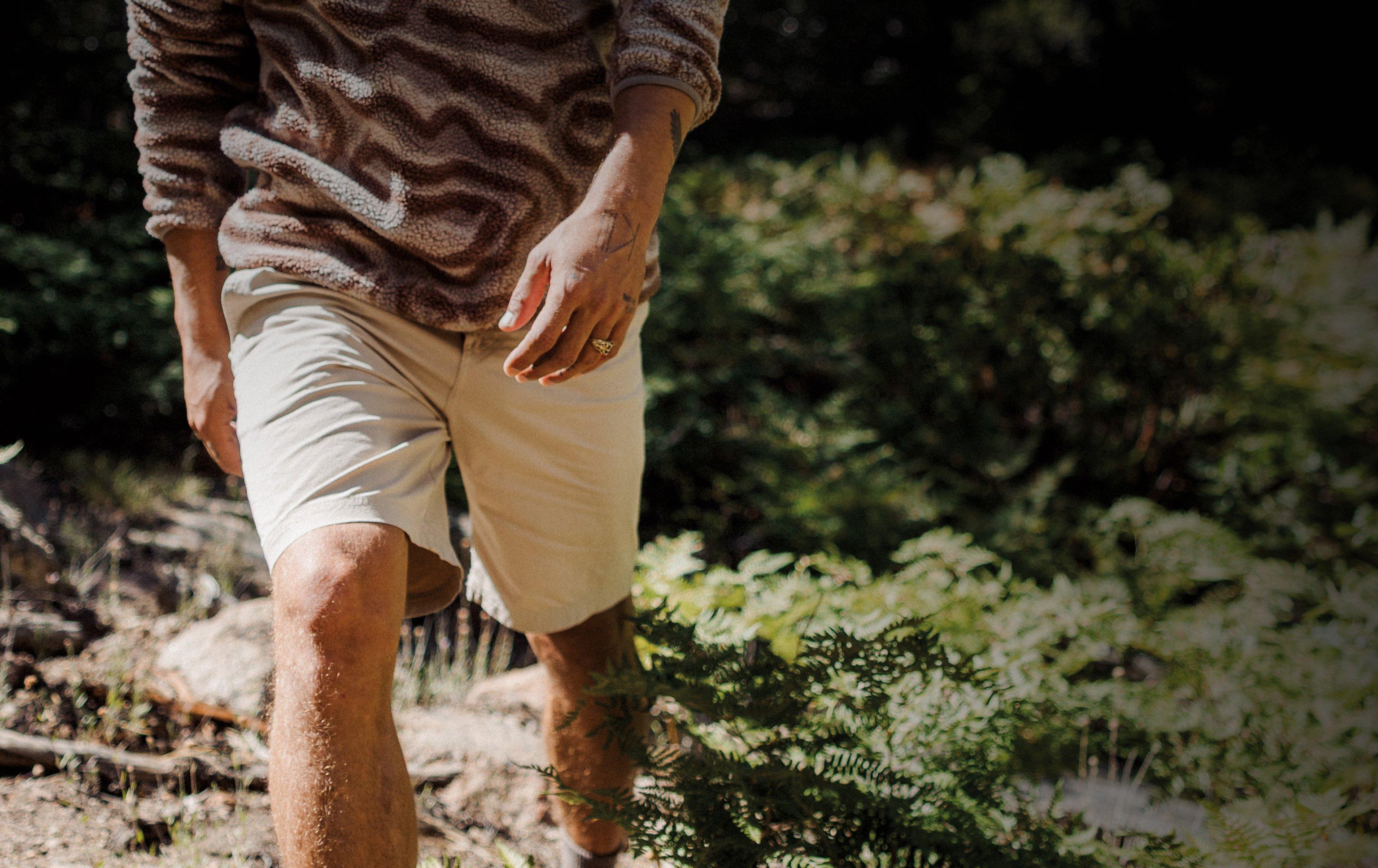 Waist-down image of a man wearing a multi-colored fleece and white shorts, walking in a forest.